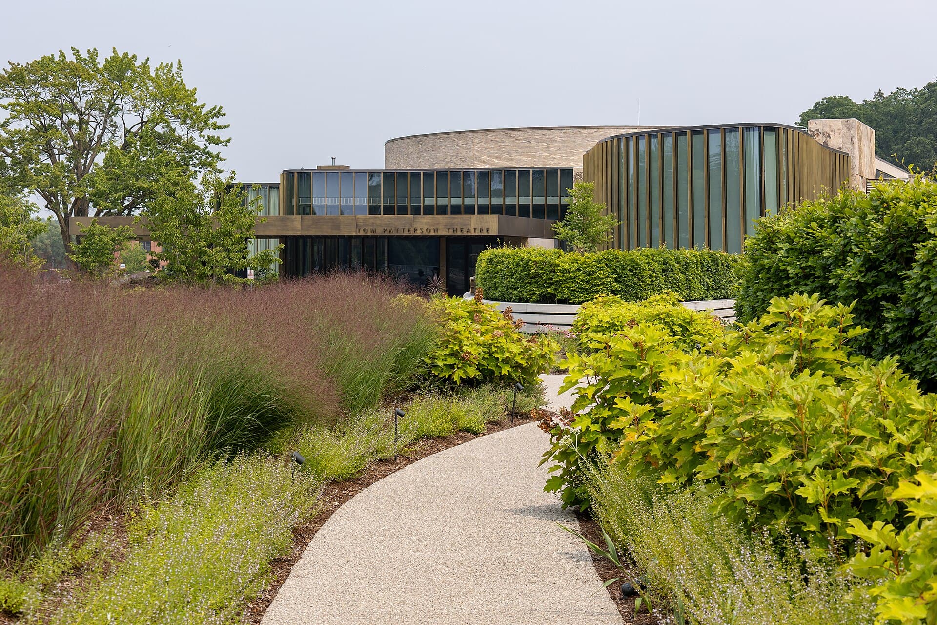 The bronze-and-glass curves of the Tom Patterson Theatre rising behind summer gardens beside the Avon River